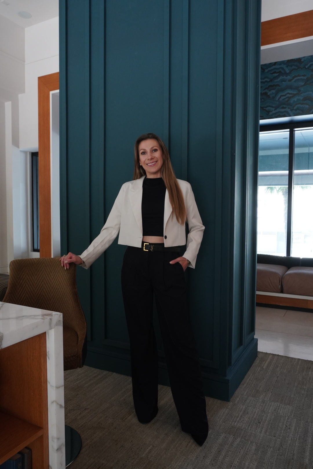 Viktoryia standing in a white blazer beside a dark architectural column.